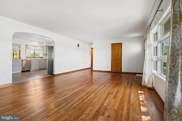 unfurnished living room featuring arched walkways, wood finished floors, and baseboards