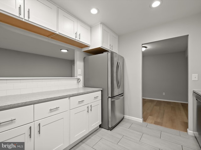 kitchen with freestanding refrigerator, white cabinets, recessed lighting, light stone countertops, and baseboards