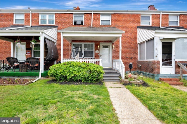 view of property featuring brick siding, a front yard, a chimney, and a porch