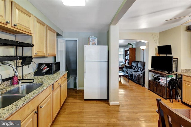 kitchen featuring freestanding refrigerator, a sink, black microwave, light wood-style flooring, and light brown cabinetry