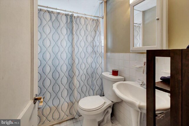 bathroom featuring tile walls, toilet, a shower with curtain, tile patterned floors, and a wainscoted wall