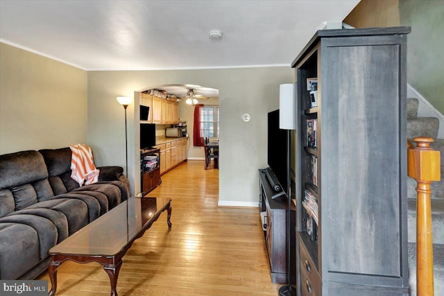 living area featuring light wood-style flooring, crown molding, ceiling fan, baseboards, and arched walkways