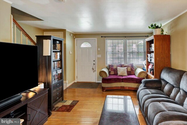 living area featuring light wood finished floors, stairway, baseboards, and ornamental molding