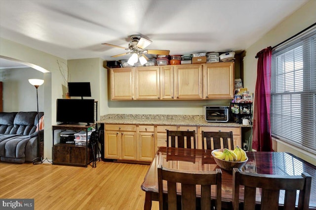 kitchen featuring light brown cabinets, ceiling fan, arched walkways, light wood finished floors, and open floor plan