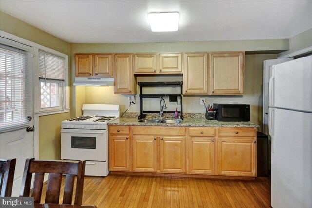 kitchen featuring white appliances, a sink, under cabinet range hood, light wood-style floors, and light stone countertops