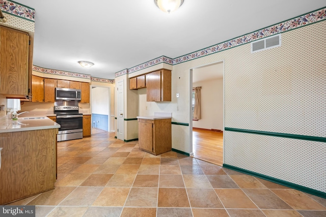 kitchen with appliances with stainless steel finishes, wallpapered walls, a sink, light countertops, and light stone finish floors