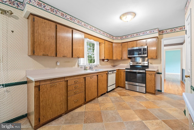 kitchen with appliances with stainless steel finishes, wallpapered walls, a sink, light countertops, and stone tile flooring