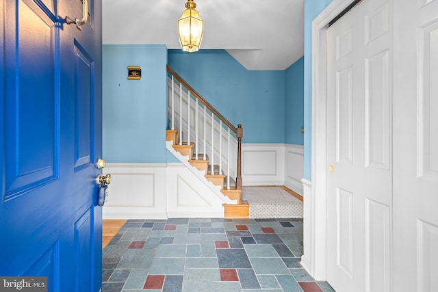 foyer entrance featuring wainscoting, a decorative wall, stairway, and dark stone finish floors