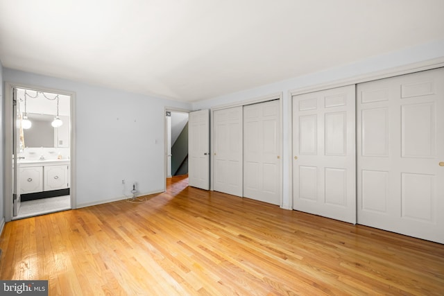 unfurnished bedroom featuring two closets, light wood finished floors, and ensuite bath
