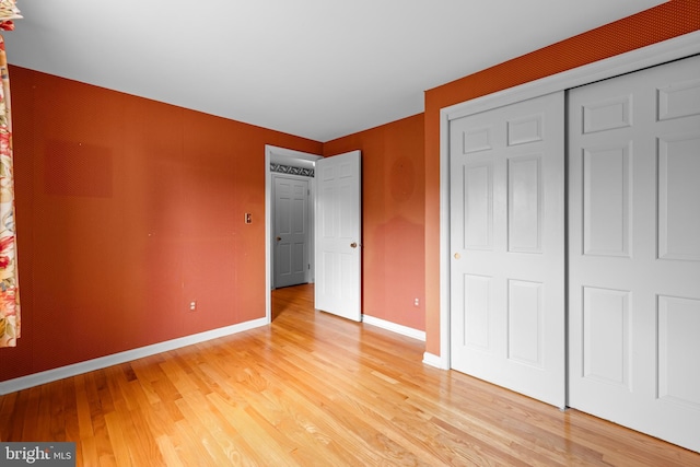 unfurnished bedroom with light wood-style flooring, baseboards, and a closet