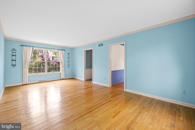 empty room featuring crown molding, light wood-type flooring, and baseboards