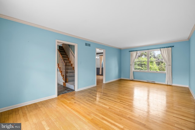 empty room featuring hardwood / wood-style flooring, baseboards, stairs, and ornamental molding