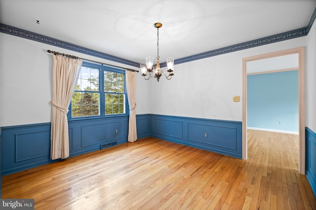 empty room with a chandelier, wainscoting, light wood finished floors, and a decorative wall