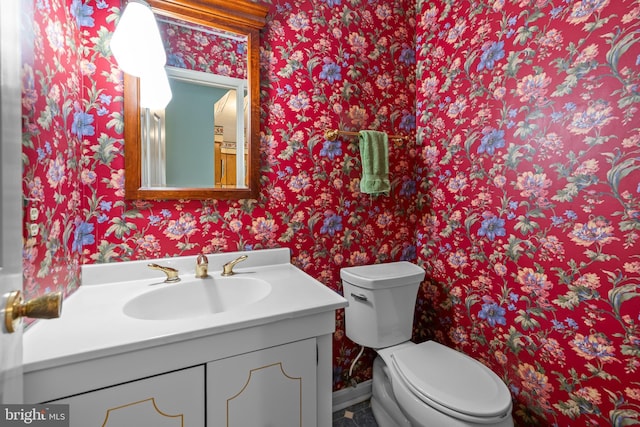 half bath with wallpapered walls, toilet, vanity, and baseboards