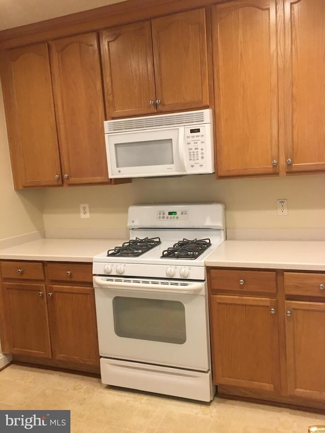 kitchen featuring white appliances, light countertops, and brown cabinetry