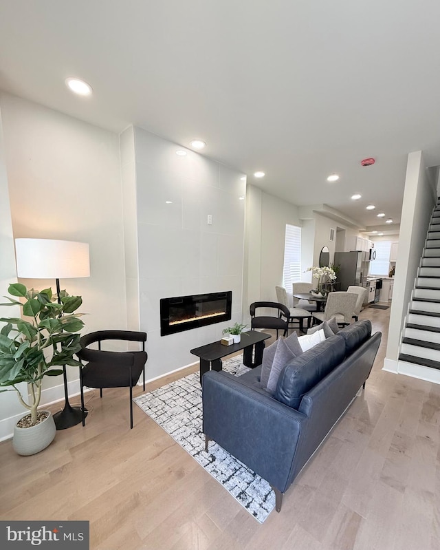 living area with a tile fireplace, stairs, baseboards, light wood-type flooring, and recessed lighting