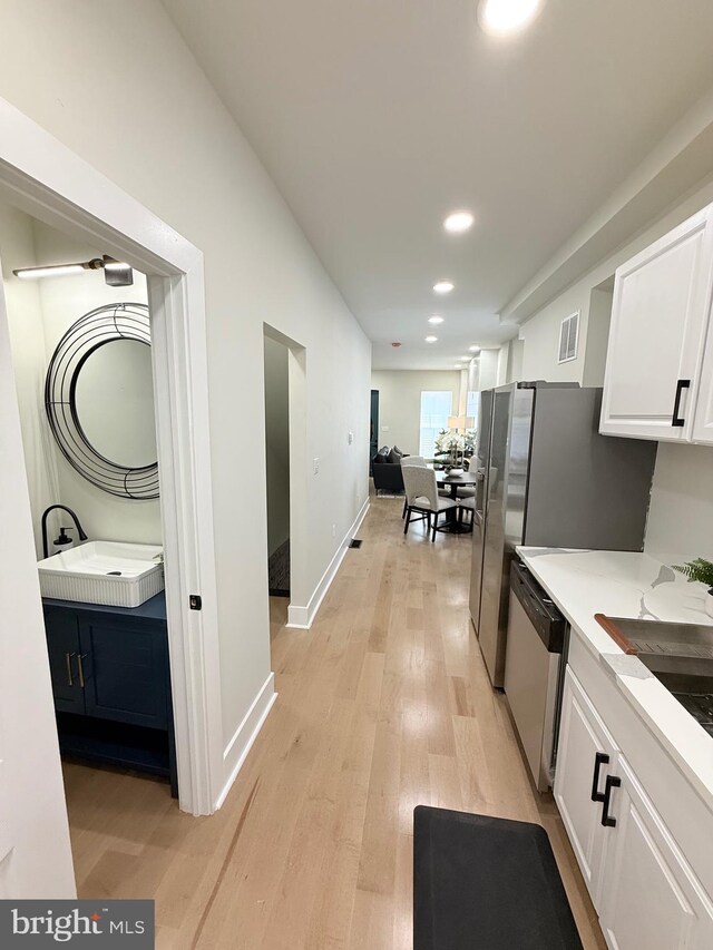 hall featuring light wood-style flooring, a sink, recessed lighting, and baseboards
