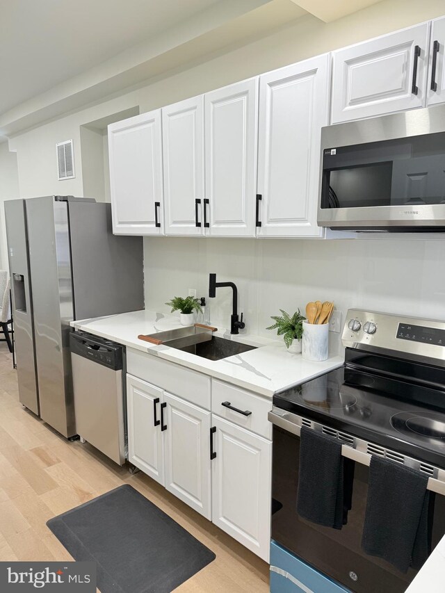 kitchen with stainless steel appliances, a sink, white cabinets, and light wood-style flooring