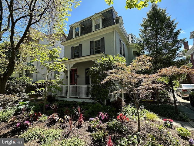 second empire-style home featuring mansard roof, stucco siding, and covered porch