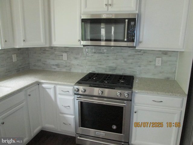 kitchen featuring appliances with stainless steel finishes, white cabinets, decorative backsplash, and light stone counters