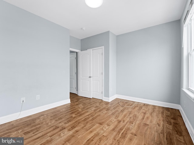 unfurnished bedroom featuring wood finished floors, baseboards, and multiple windows