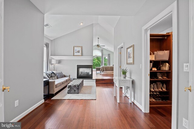 living room with lofted ceiling, a ceiling fan, wood finished floors, a glass covered fireplace, and baseboards