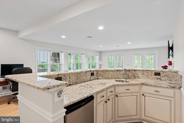 kitchen featuring stainless steel dishwasher, a sink, cream cabinetry, light stone counters, and light wood-style floors