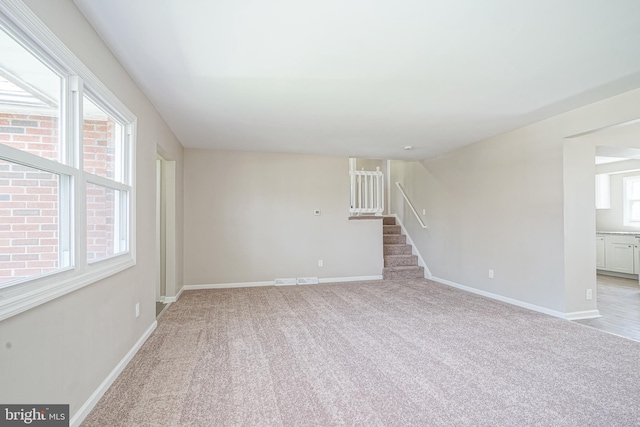 unfurnished room with stairway, baseboards, and light colored carpet