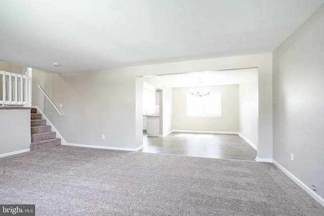 unfurnished room featuring carpet, a chandelier, stairs, and baseboards
