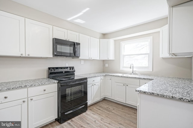 kitchen with black appliances, a sink, light wood finished floors, white cabinetry, and light stone counters