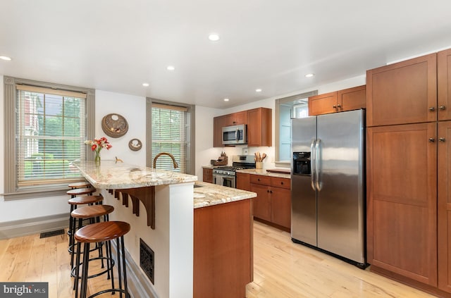 kitchen with stainless steel appliances, a breakfast bar, recessed lighting, light wood-style floors, and light stone countertops