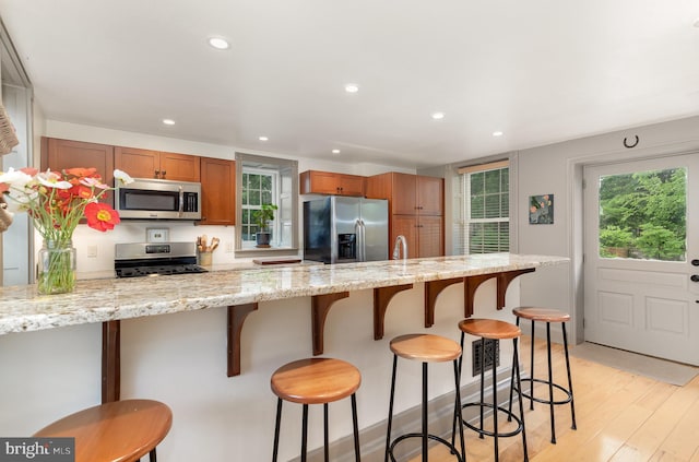 kitchen featuring stainless steel appliances, light wood-style flooring, brown cabinetry, recessed lighting, and a breakfast bar