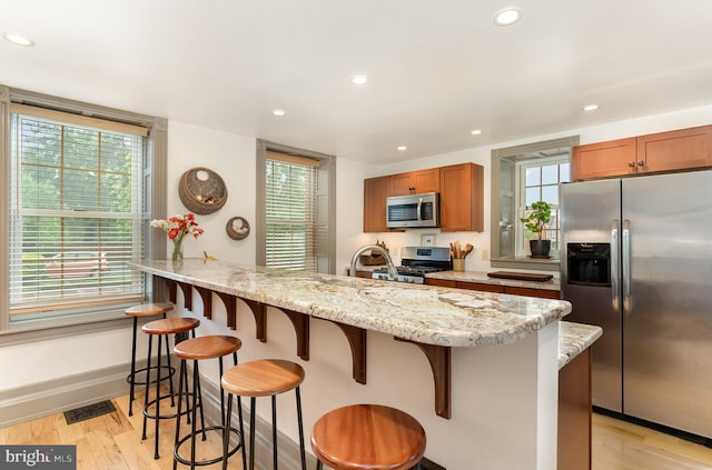 kitchen featuring appliances with stainless steel finishes, light wood-type flooring, recessed lighting, brown cabinetry, and a breakfast bar