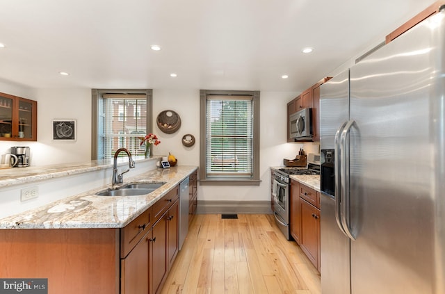 kitchen featuring stainless steel appliances, a sink, baseboards, light wood-style floors, and glass insert cabinets
