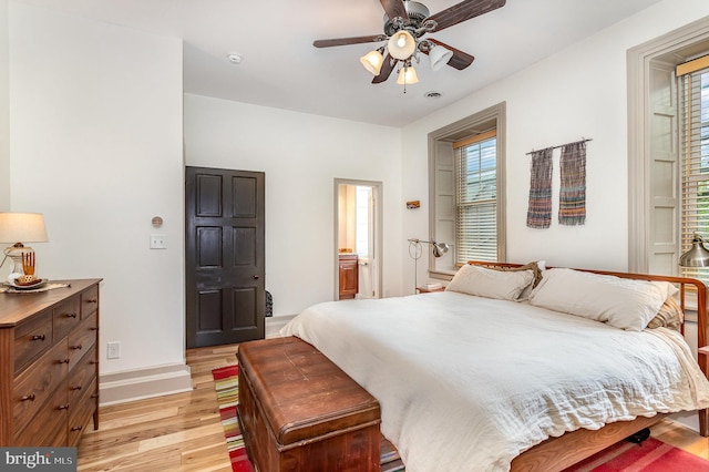 bedroom featuring light wood-style floors, baseboards, ceiling fan, and ensuite bath