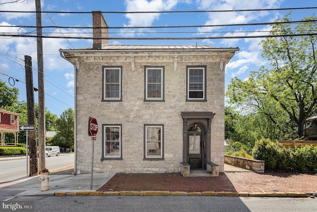 view of front of house featuring a chimney, stone siding, a standing seam roof, and metal roof