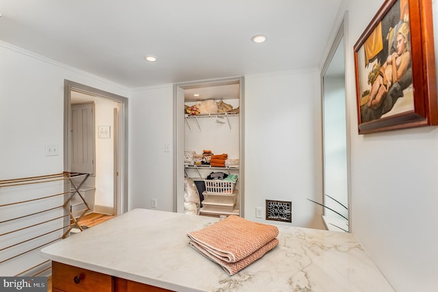 bedroom featuring recessed lighting, a walk in closet, ornamental molding, a closet, and wood finished floors