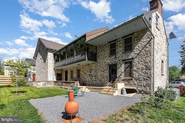 rear view of property featuring a balcony, stone siding, a lawn, and metal roof