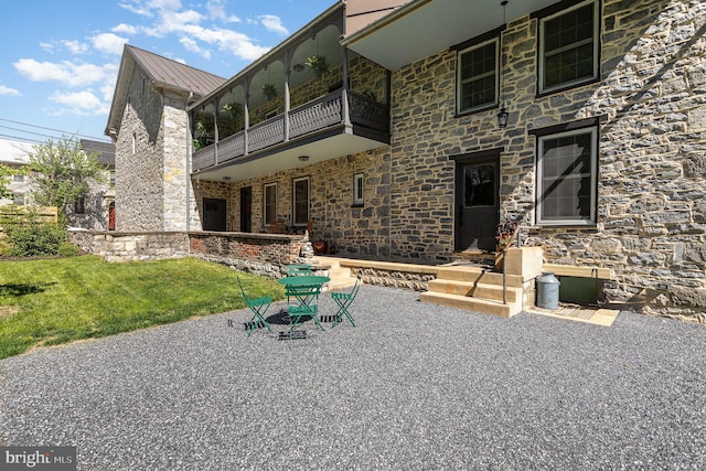 rear view of house with a balcony, stone siding, a lawn, and metal roof