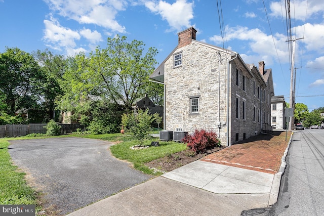 view of side of property with stone siding, central air condition unit, a chimney, and fence