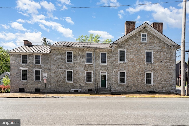 view of front of house with a standing seam roof, a chimney, entry steps, metal roof, and stone siding