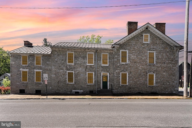 view of front facade featuring a standing seam roof, a chimney, crawl space, metal roof, and stone siding