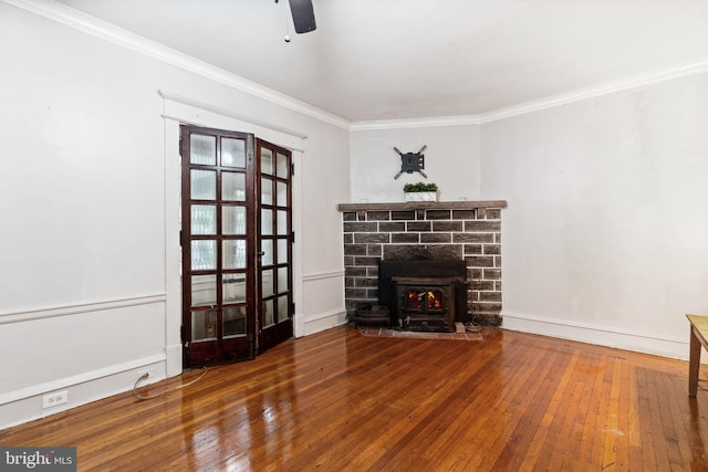 unfurnished living room with wood-type flooring, ornamental molding, ceiling fan, a wood stove, and baseboards