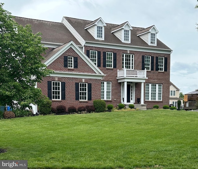 colonial house with brick siding, a front yard, a balcony, and a shingled roof