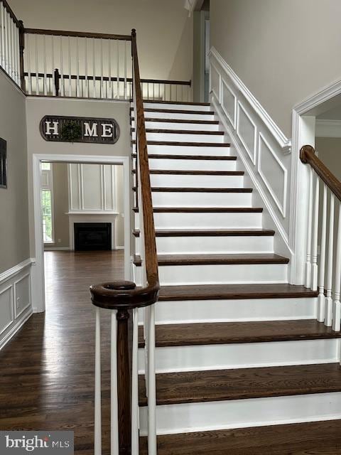 staircase featuring wood finished floors, a decorative wall, a fireplace, and wainscoting
