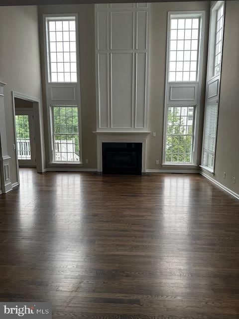 unfurnished living room featuring a towering ceiling, a fireplace, plenty of natural light, dark wood-style flooring, and baseboards
