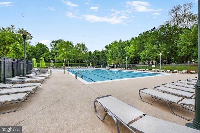 community pool with fence, a patio, and view of wooded area