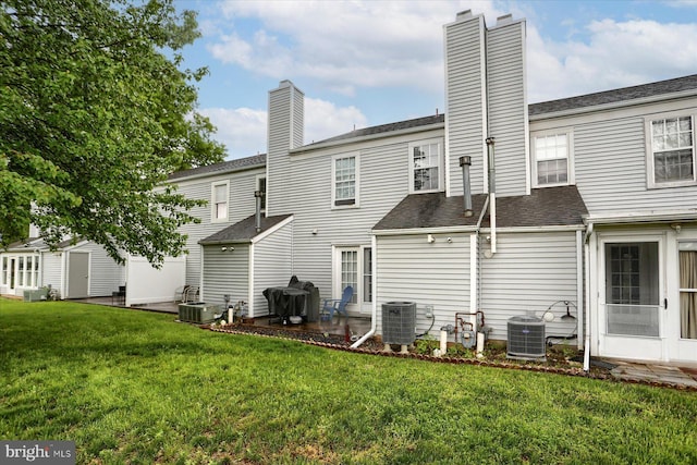 back of property with central AC, a yard, a shingled roof, and a chimney