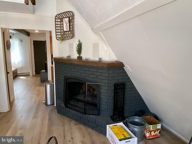 detailed view of wood finished floors, a fireplace, a baseboard heating unit, baseboards, and beamed ceiling