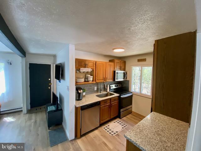 kitchen featuring stainless steel appliances, a sink, light wood-style floors, a textured ceiling, and brown cabinetry